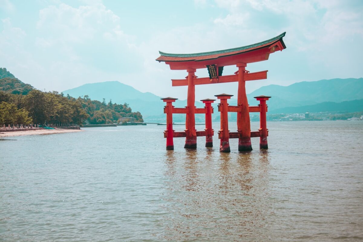 A red torii gate in the water with a shrine in the background