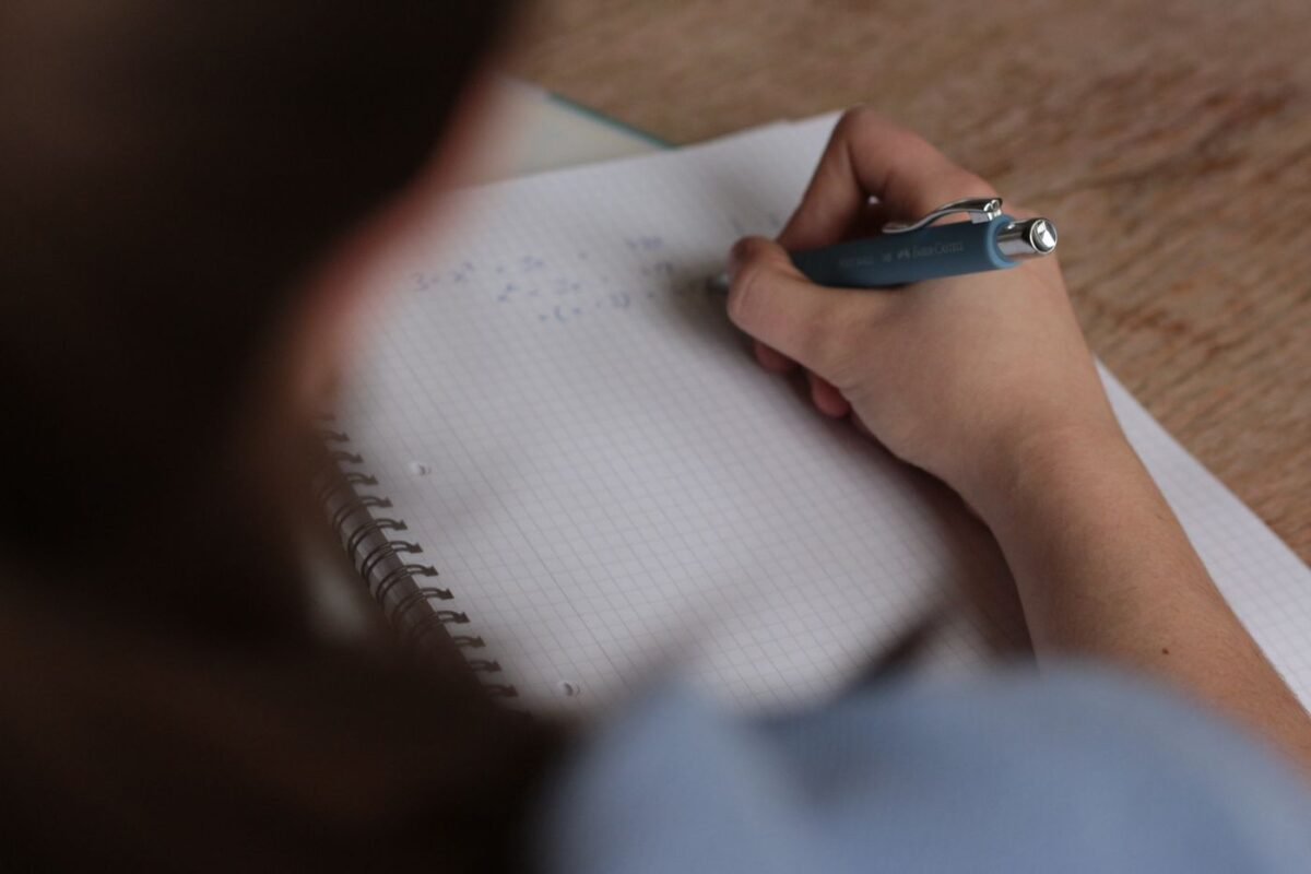 Close-up of a hand writing homework notes with a pen in a notebook