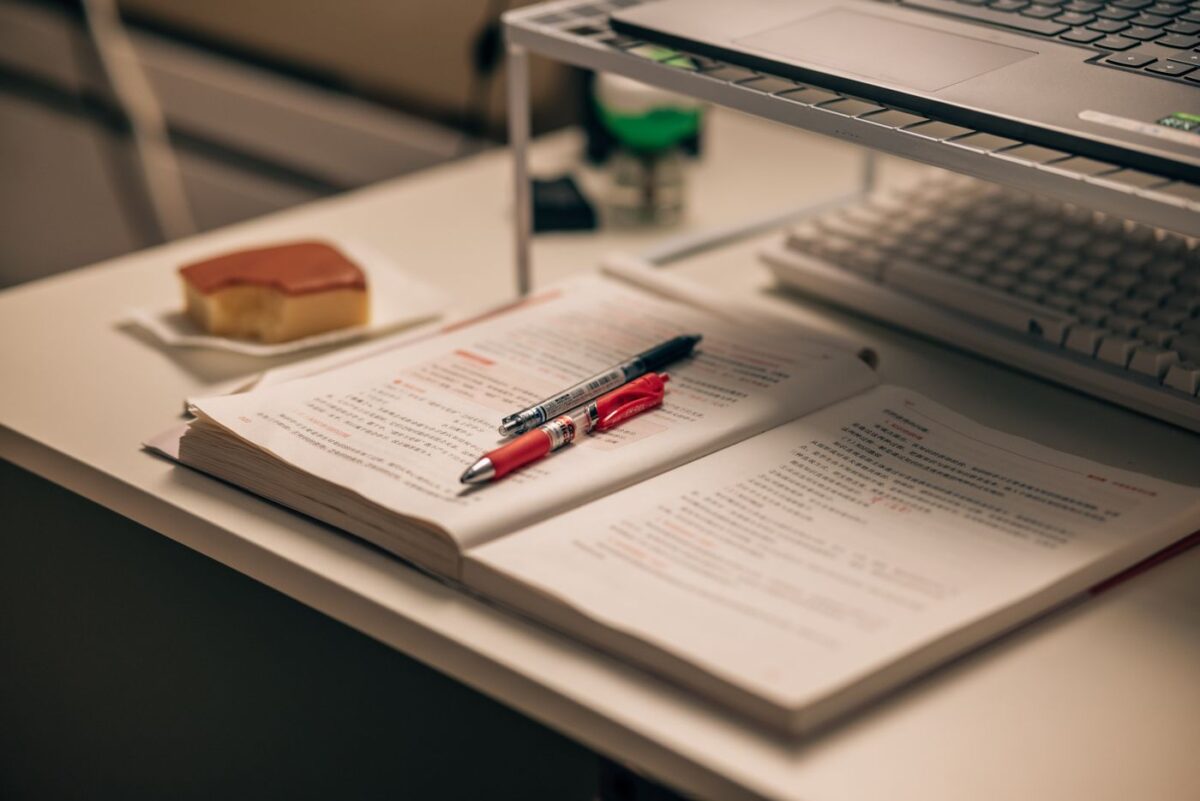 Open book with study notes, pens and a laptop on a desk