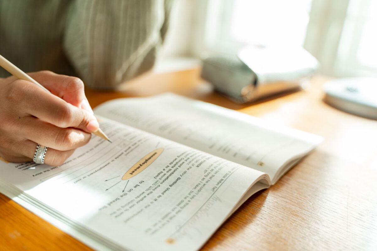 Student taking notes from a textbook at a sunlit desk