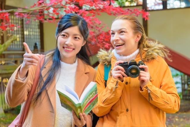 “Sumimasen” in Japan: The One Japanese Word Every Traveller Should Know Two women travellers in autumn coats, one holding a guidebook and pointing, the other with a camera